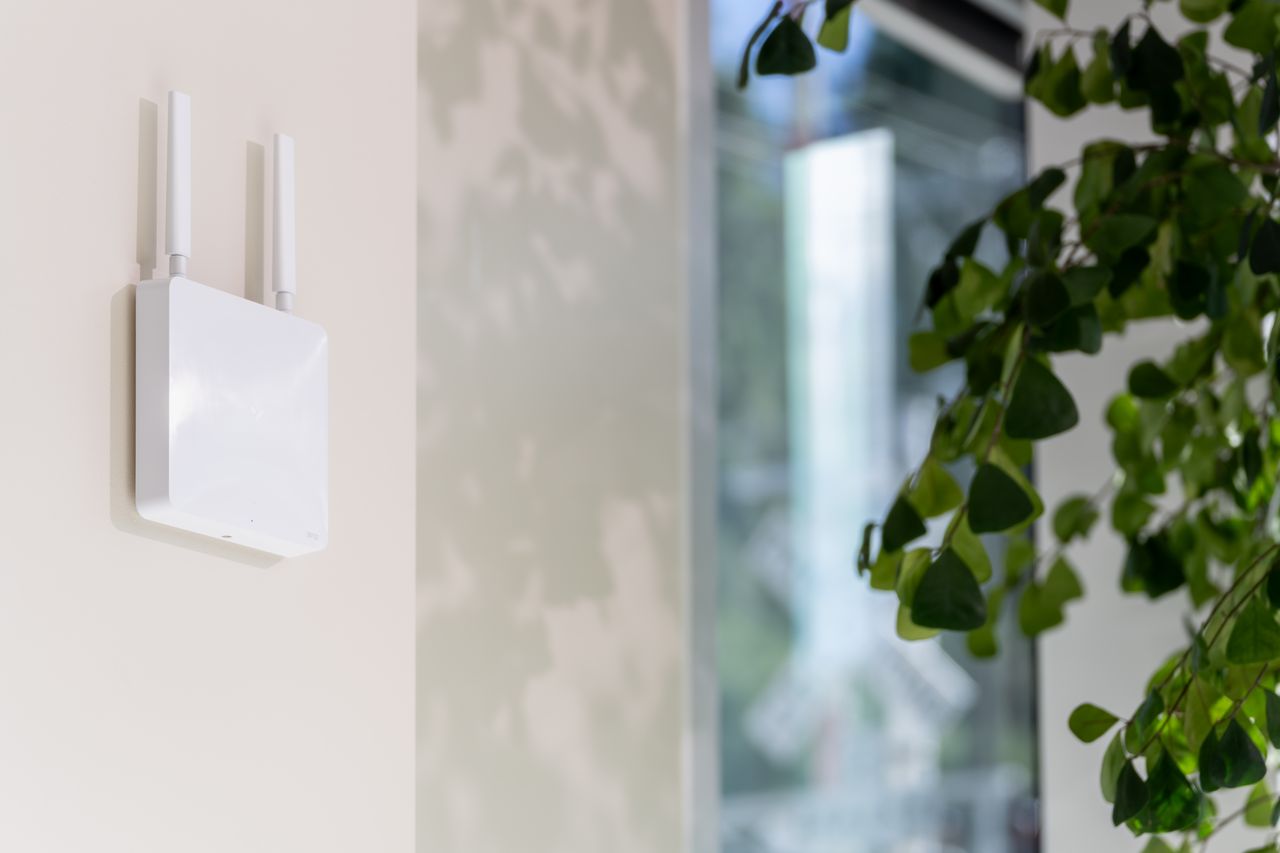 A white wall-mounted wireless access point with three antennas installed indoors.