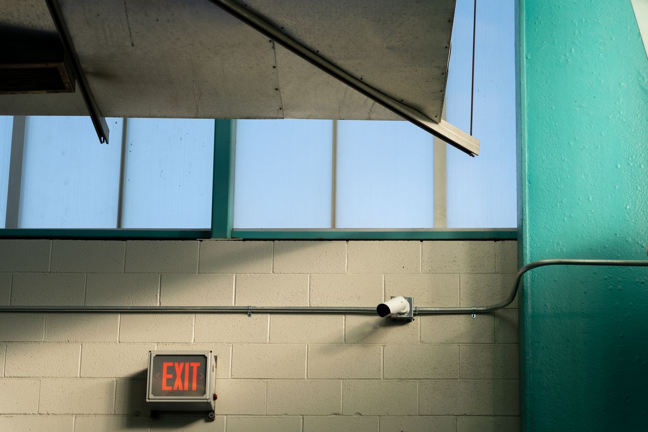 Verkada bullet camera mounted on interior cinderblock wall near an exit sign.