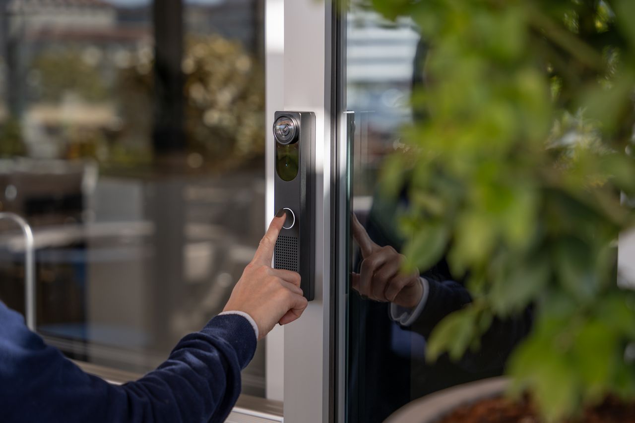 A person pressing the button on a Verkada intercom mounted beside a glass door.