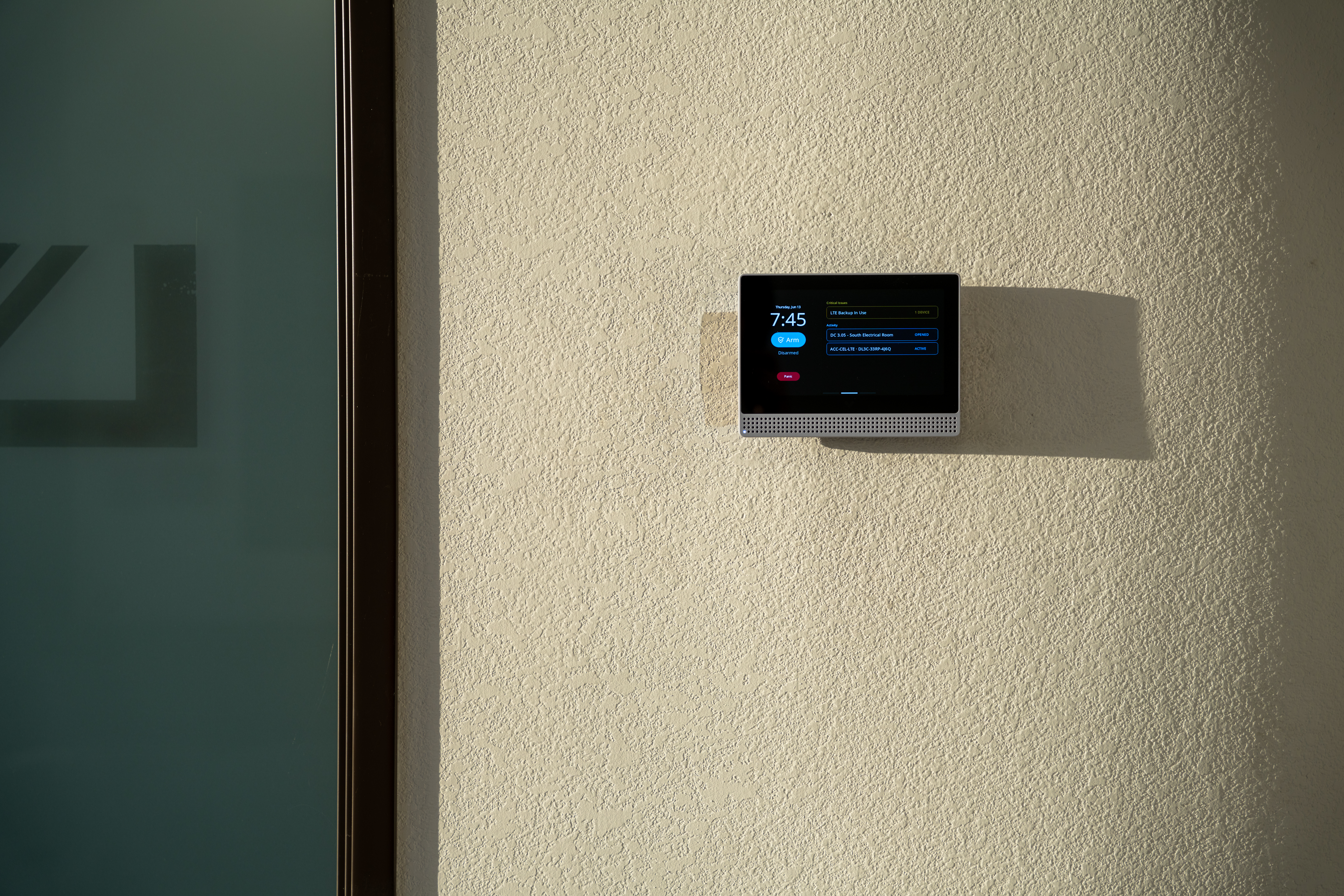 Verkada alarm panel mounted on a textured interior wall next to a glass door.