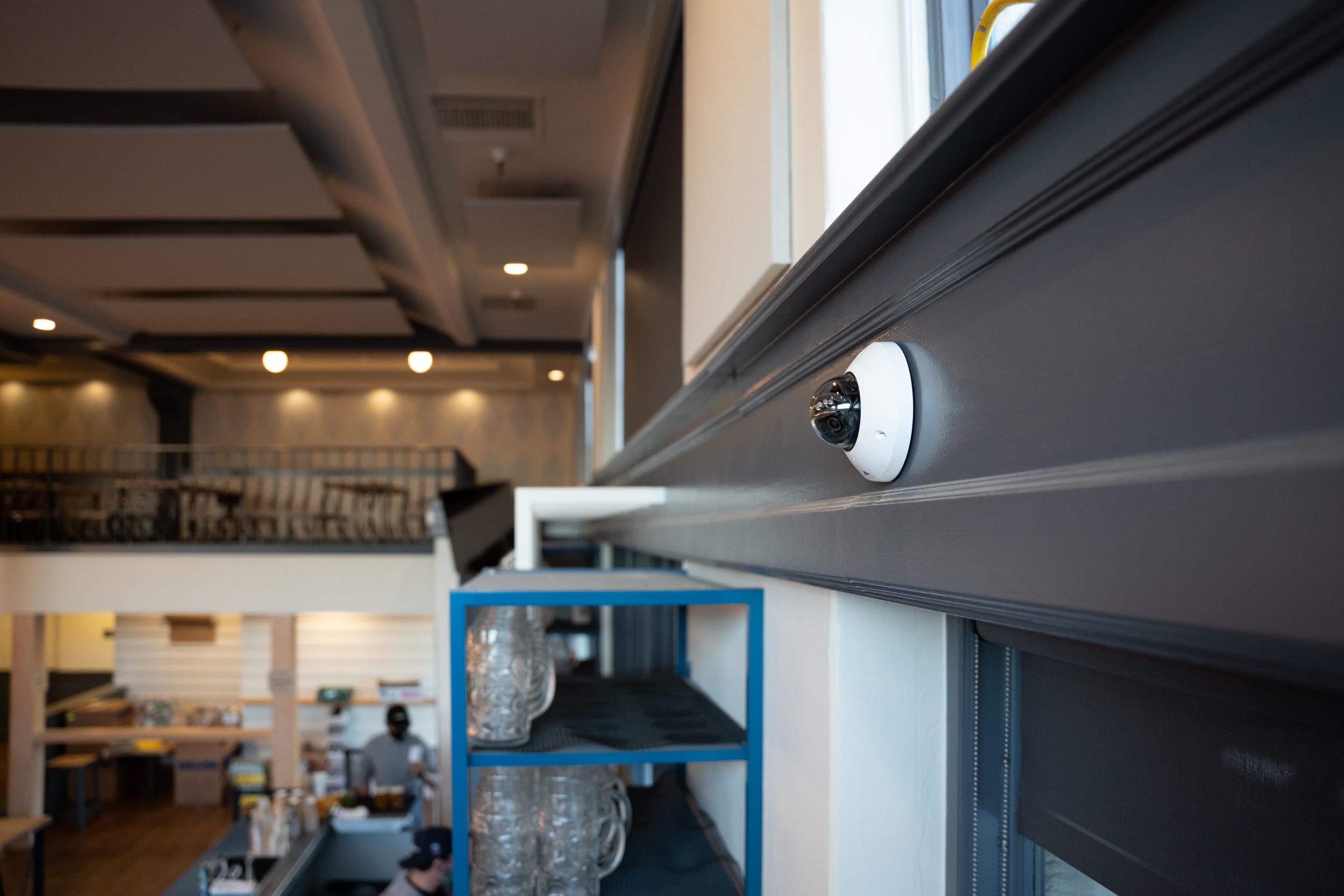 Verkada mini dome camera mounted on a gray beam inside a restaurant.
